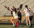 Female athletes competing in a flag football game, with one player reaching for a pass near the goal line.
