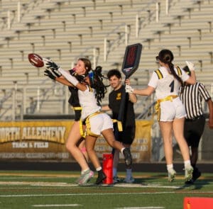 Female athletes competing in a flag football game, with one player reaching for a pass near the goal line.