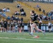 Player 13 running with a football during a flag football game, surrounded by cheering teammates and spectators.