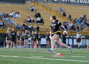 Player 13 running with a football during a flag football game, surrounded by cheering teammates and spectators.