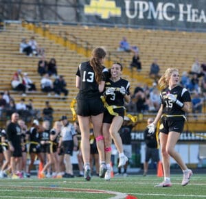 Cheering players celebrate a touchdown during a flag football game, showcasing teamwork and school spirit on the field.