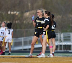 Two female athletes in black jerseys strategizing on the field during a flag football game, showcasing team spirit.