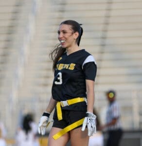 Cheerful female player in a black sports uniform, smiling on the field during a flag football game.