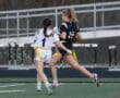 Two female athletes compete in a flag football game, one attempting to evade the other while holding the ball.
