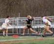 Female players compete in a flag football game, with one sprinting past opponents while holding the ball.