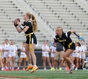 Girls' flag football game: player prepares to pass while teammate moves to receive the ball on the field.