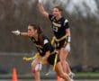Two female flag football players in black uniforms signal during a game, demonstrating teamwork and athleticism on the field.