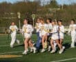 Group of female lacrosse players in white uniforms running on the field, showcasing teamwork and athletic spirit.