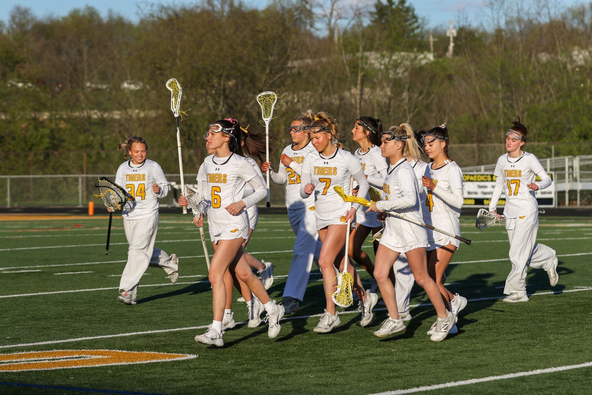 Group of female lacrosse players in white uniforms running on the field, showcasing teamwork and athletic spirit.
