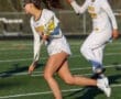 Two female lacrosse players in action on a field, showcasing athleticism and teamwork in sports attire.