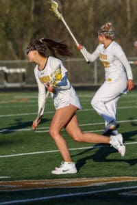 Two female lacrosse players in action on a field, showcasing athleticism and teamwork in sports attire.