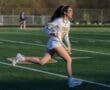 A female lacrosse player in action on the field wearing a Tigers uniform and a protective headgear.