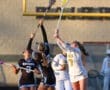 High school girls' lacrosse players compete for the ball during an evening match on the field.