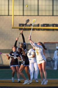 High school girls' lacrosse players compete for the ball during an evening match on the field.