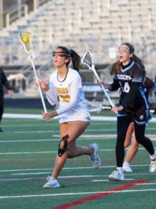 High school girls' lacrosse match with players in action on the field, showcasing teamwork and competitive spirit.