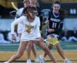 Two female lacrosse players compete for the ball on a field, showcasing athleticism and teamwork during a game.