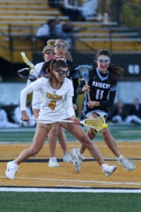 Two female lacrosse players compete for the ball on a field, showcasing athleticism and teamwork during a game.