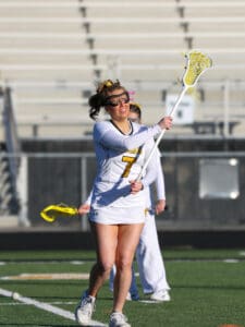 Girl lacrosse player in action on the field, wearing team colors and gear, preparing to make a play during practice.