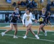 Lacrosse players compete fiercely as the Tigers and Raiders clash on the field during a dynamic match.