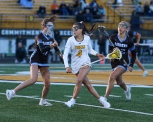 Lacrosse players compete fiercely as the Tigers and Raiders clash on the field during a dynamic match.