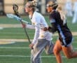 Two female lacrosse players sprint on the field, focused on the game, showcasing teamwork and athleticism.