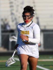 Lacrosse player in a white Tigers uniform running on the field with a lacrosse stick, focused and determined.