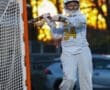 Female lacrosse goalie in action during sunset, wearing jersey number 34, focused on defending the goal.