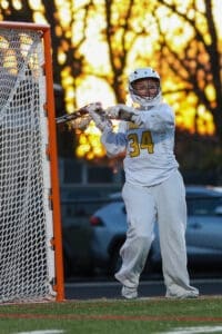 Female lacrosse goalie in action during sunset, wearing jersey number 34, focused on defending the goal.