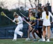 Female lacrosse players in action during a game, showcasing teamwork and athleticism on the field at dusk.