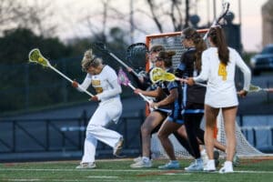 Female lacrosse players in action during a game, showcasing teamwork and athleticism on the field at dusk.