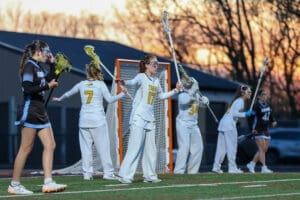 Girls' lacrosse game at sunset, players in uniforms preparing for play on the field, showcasing teamwork and athleticism.