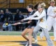 High school girls lacrosse players compete for the ball in an intense match under stadium lights.