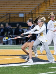 High school girls lacrosse players compete for the ball in an intense match under stadium lights.