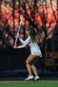 Female lacrosse player in action during sunset, showcasing athleticism and focus on the field.
