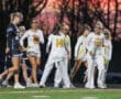 Girls' lacrosse team celebrating on the field at sunset, showcasing teamwork and sportsmanship.