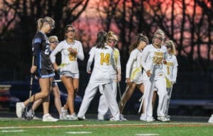 Girls' lacrosse team celebrating on the field at sunset, showcasing teamwork and sportsmanship.