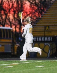 Lacrosse player in uniform runs on the field at sunset, showcasing athleticism and team spirit in a vibrant game setting.