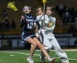 Lacrosse players compete fiercely under the lights during a high school match, showcasing athletic skill and teamwork.
