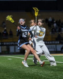 Lacrosse players compete fiercely under the lights during a high school match, showcasing athletic skill and teamwork.