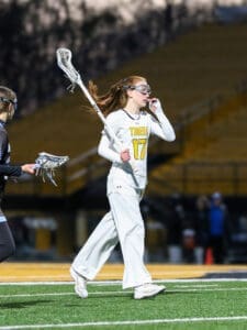 Lacrosse player in a Tigers uniform walks on the field, holding a stick with determination during a nighttime game.