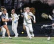 Girls' lacrosse game action with players in motion, showcasing teamwork and athleticism on a turf field.