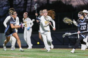 Girls' lacrosse game action with players in motion, showcasing teamwork and athleticism on a turf field.