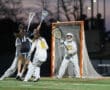 Action shot of a women’s lacrosse game, featuring a player taking a shot on goal while the goalie prepares to defend.