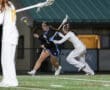 Two female lacrosse players compete for a ball during an evening match, showcasing athleticism and teamwork.