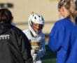 Young lacrosse player in helmet engages with teammates and coaches during practice, showcasing teamwork and focus.