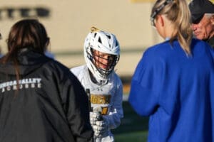 Young lacrosse player in helmet engages with teammates and coaches during practice, showcasing teamwork and focus.