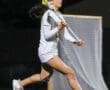 High school lacrosse player running with a stick during a night game, focused and ready to make a play.