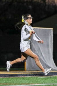High school lacrosse player running with a stick during a night game, focused and ready to make a play.