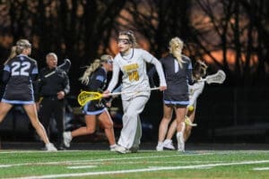 Lacrosse game in action at dusk, featuring players in motion on the field, showcasing teamwork and athleticism.