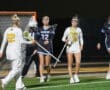 High school lacrosse players in action on a night field, showcasing teamwork and competitive spirit during a game.